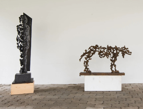 Two abstract metal sculptures on separate platforms; one resembles a standing human figure, the other resembles an animal, displayed against a plain white wall.