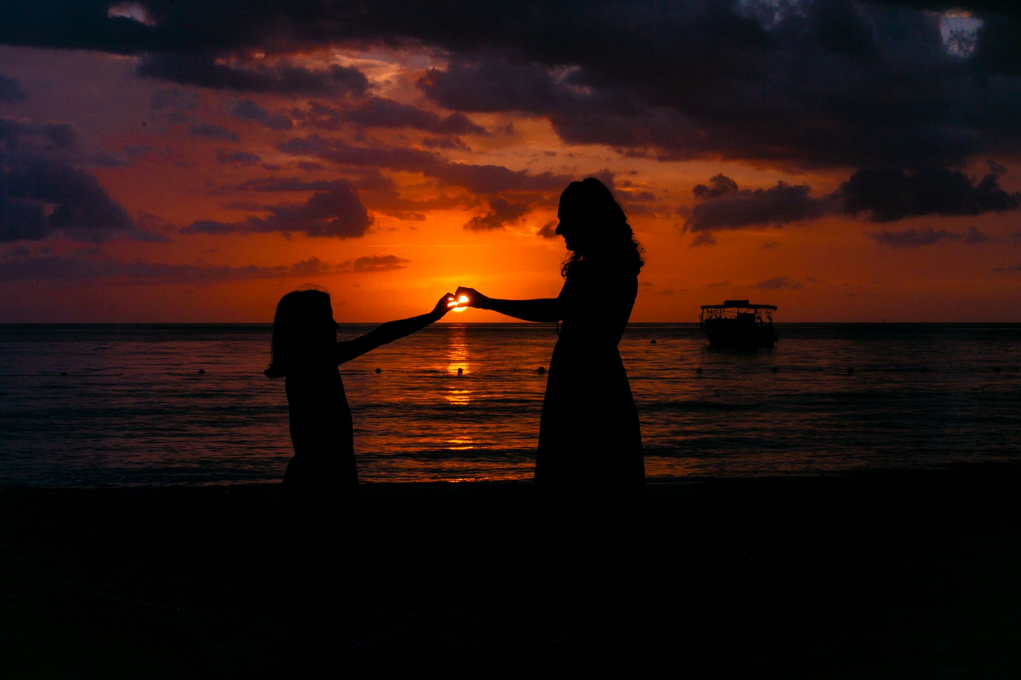 two girls connecting their hands with each other to make a heart over the sunset