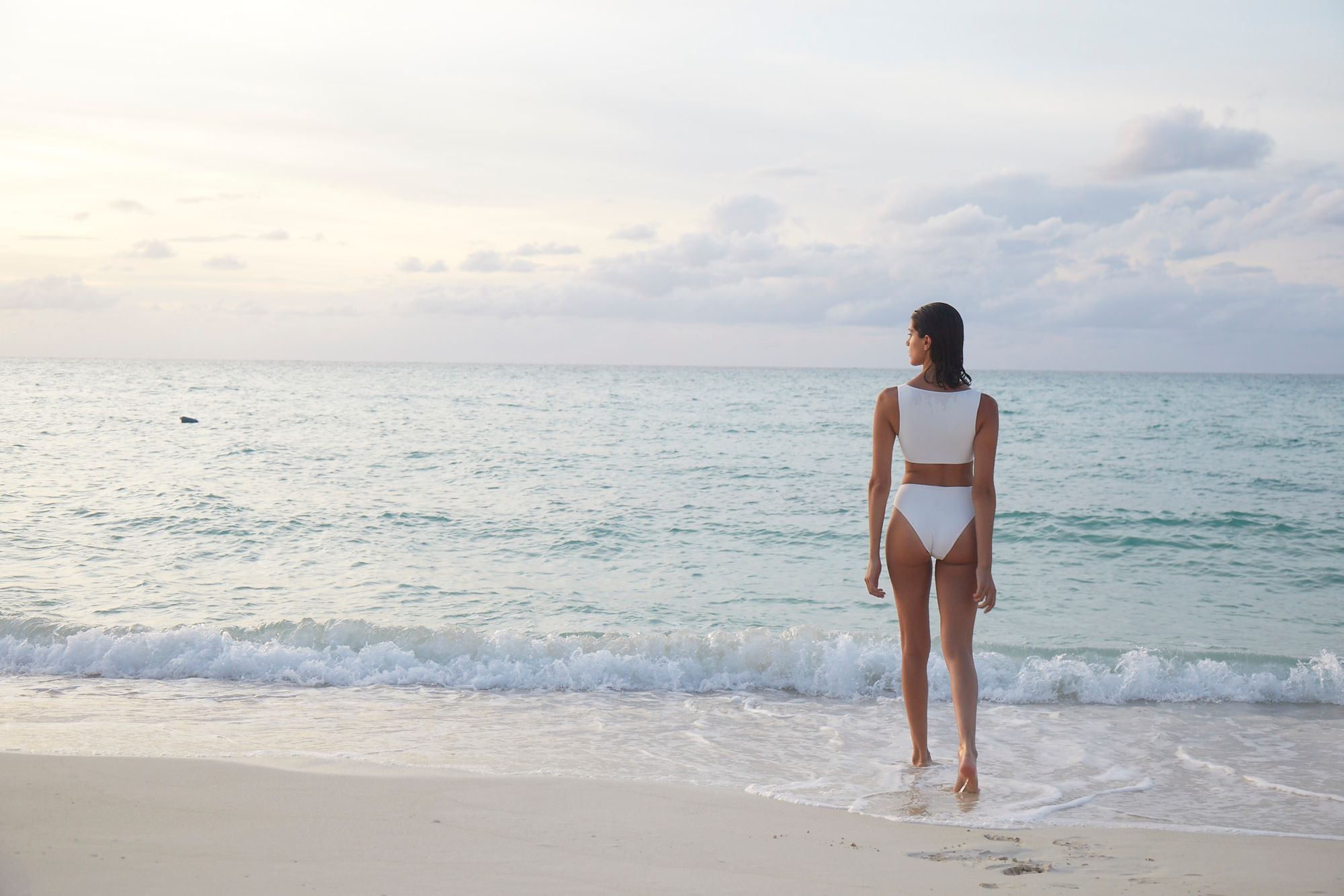 woman in white bikini standing on the shore of love beach staring out into the ocean